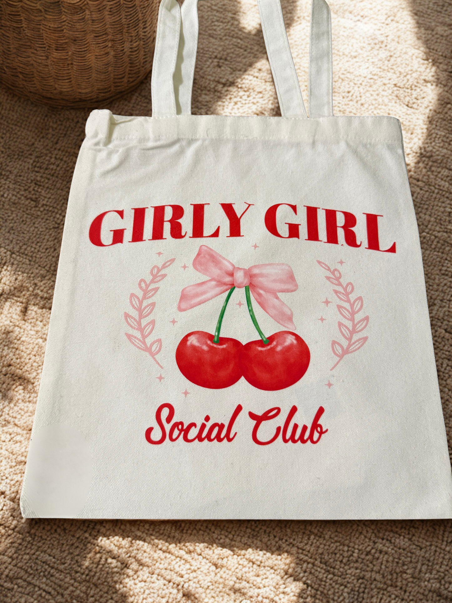Tote bag with 'Girly Girl Social Club' design featuring cherries and a bow on a textured surface.