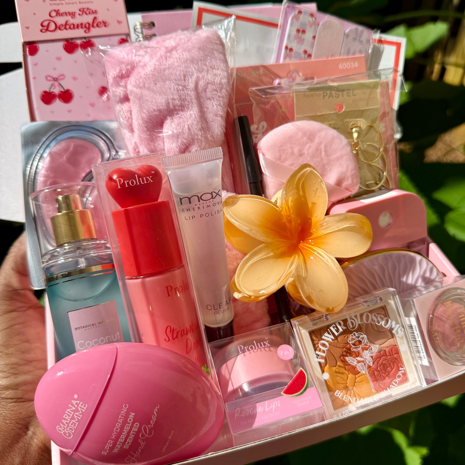 Collection of beauty products including lip gloss, serum, and flower in a box 
